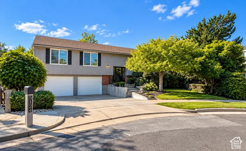 Split-level residence featuring a two-car garage, mature trees, and a concrete driveway