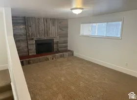 Carpeted room featuring a fireplace with a wood-panel surround and hearth, a window with blinds, and white walls