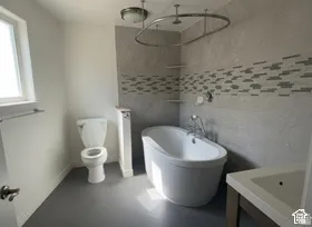 Freestanding soaking tub with chrome fixtures, floor-to-ceiling textured wall tile, and decorative mosaic tile accent