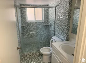 Walk-in shower with glass enclosure, mosaic tile surround, built-in shelving, and a vanity with an integrated sink