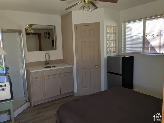 Wood-finish flooring, ceiling fan, vanity with integrated sink, glass block accent window, and mini-refrigerator