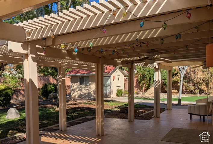 Expansive covered patio featuring a slatted pergola, ceiling fan, and concrete paver flooring