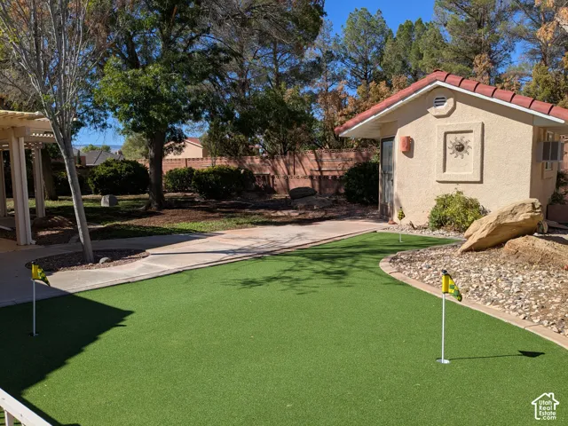 Putting green with two holes, concrete pathways, and a detached structure featuring a red tile roof and stucco exterior