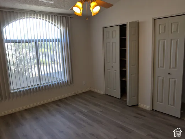 Arch-top window with vertical blinds, wood-finish flooring, ceiling fan with integrated lighting, and bi-fold closet doors