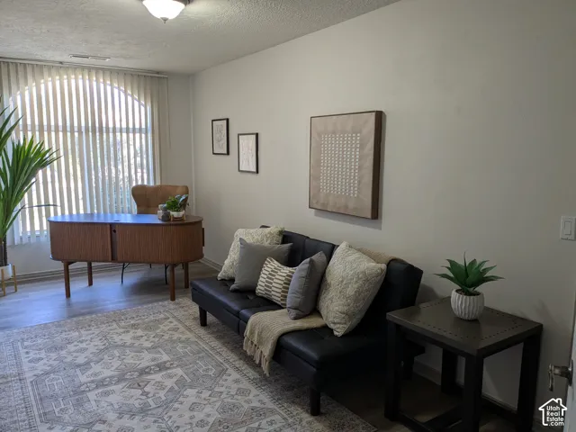 Arched window with vertical blinds, neutral wall paint, wood-finish flooring, ceiling-mounted light fixture, and a built-in wood desk