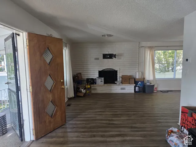 Wood-finish flooring throughout, featuring a white brick fireplace with a black firebox, a wall-mounted fixture, and an entry door with diamond-patterned glass inserts