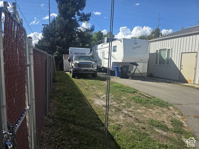 Chain-link fence with privacy slats, grassy strip, asphalt driveway, and a white corrugated metal building with a window and solid door