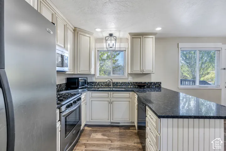 Kitchen featuring stainless steel appliances, dark stone countertops, mosaic tile backsplash, and wood-finish flooring