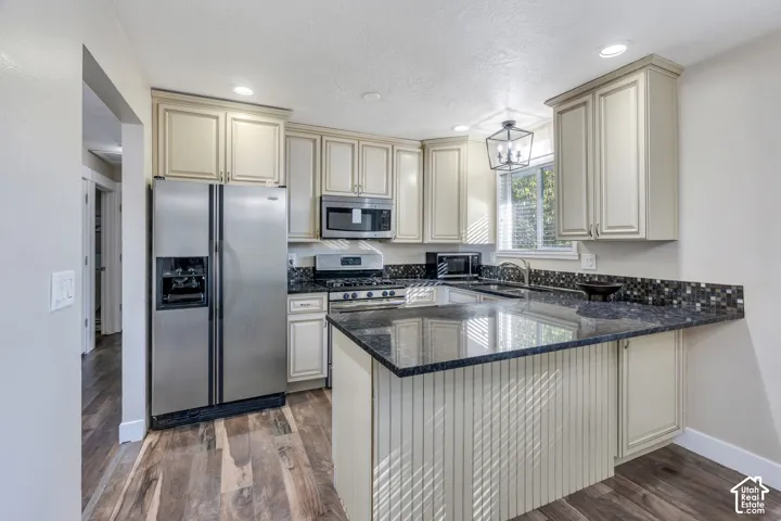 Kitchen featuring wood-finish flooring, recessed lighting, light-toned cabinetry, stainless steel appliances, and dark speckled countertops
