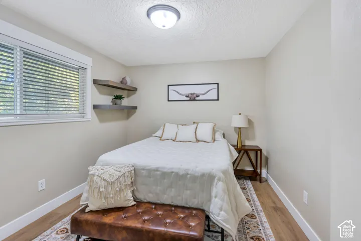 Recessed window with horizontal blinds, wood-finish flooring, two floating wall shelves, and an overhead flush-mount ceiling light