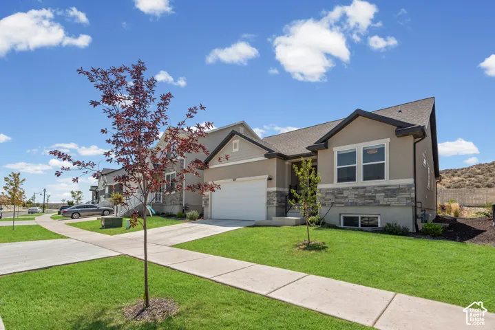 Stucco exterior with stone accenting, dark shingle roof, attached garage, concrete driveway, and manicured lawn