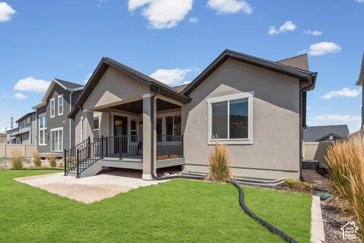 Expansive green lawn with a covered porch featuring black railings, a concrete patio, and a stucco exterior with a dark roof