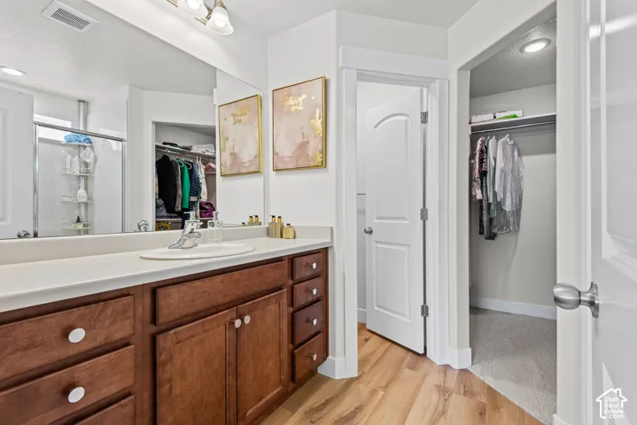 Wood-finish flooring, white countertop vanity with integrated sink, wood cabinetry, and a walk-in shower with a glass enclosure