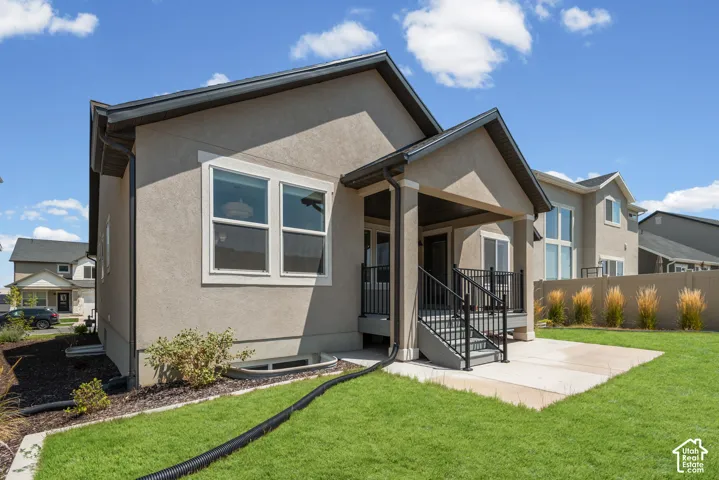 Stucco exterior, covered patio, concrete patio, green lawn, and dark-framed windows