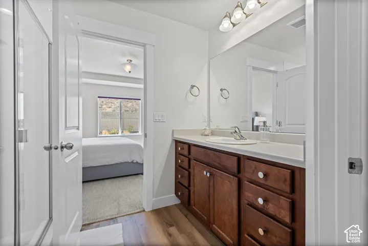 Wood-finish flooring, wood cabinetry, built-in vanity with integrated sink, expansive vanity mirror, and overhead vanity lighting
