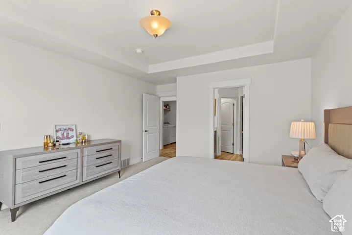 Spacious primary bedroom featuring a tray ceiling with recessed lighting, dual walk-in closets, and a coordinating dresser with multiple drawers