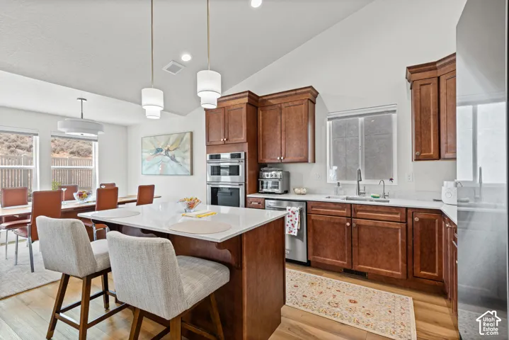 Vaulted ceiling with pendant lighting, wood-finish flooring, white countertops, built-in stainless steel double ovens, and shaker-style wood cabinetry