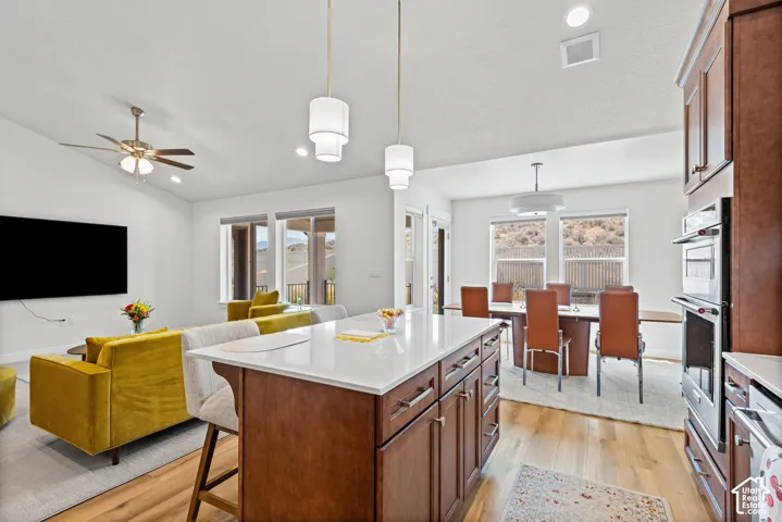Kitchen island with seating and white countertop, hardwood-style flooring, white walls, recessed lighting, and built-in double ovens