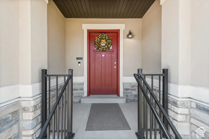 Stucco exterior with stone accent detailing, a red entry door, wrought iron railings, and an outdoor wall sconce