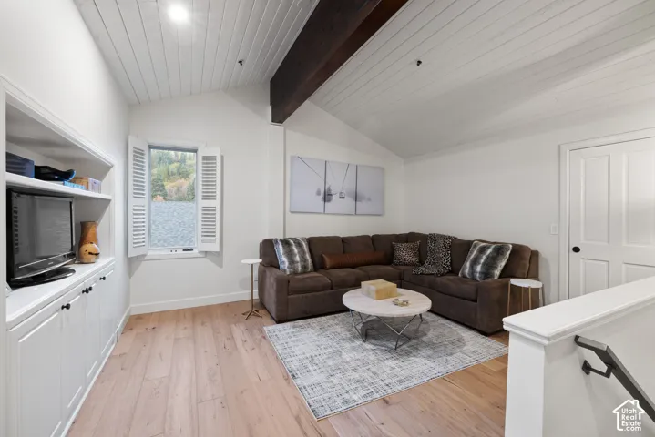 Vaulted ceiling with wood paneling and exposed beam, wood-finish flooring, built-in cabinetry with open shelving, and a paneled door