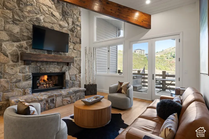 Stone-clad fireplace with a wood mantel, wood-finish flooring, exposed wood beam, and French doors leading to an outdoor space