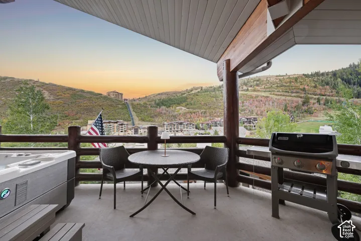 Outdoor balcony featuring a hot tub, log railing, overhead wood beam, and mountain scenery
