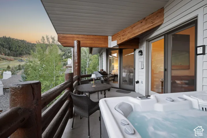 Private balcony featuring a built-in hot tub, log railing, and direct access to an interior room through sliding glass doors