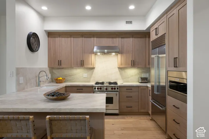 Kitchen featuring wood-finish cabinetry, stainless steel appliances, stone countertops, and wood-finish flooring
