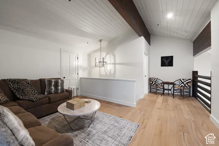 Vaulted ceiling with exposed wood beams, wood-finish flooring, white shiplap ceiling, and a contemporary chandelier