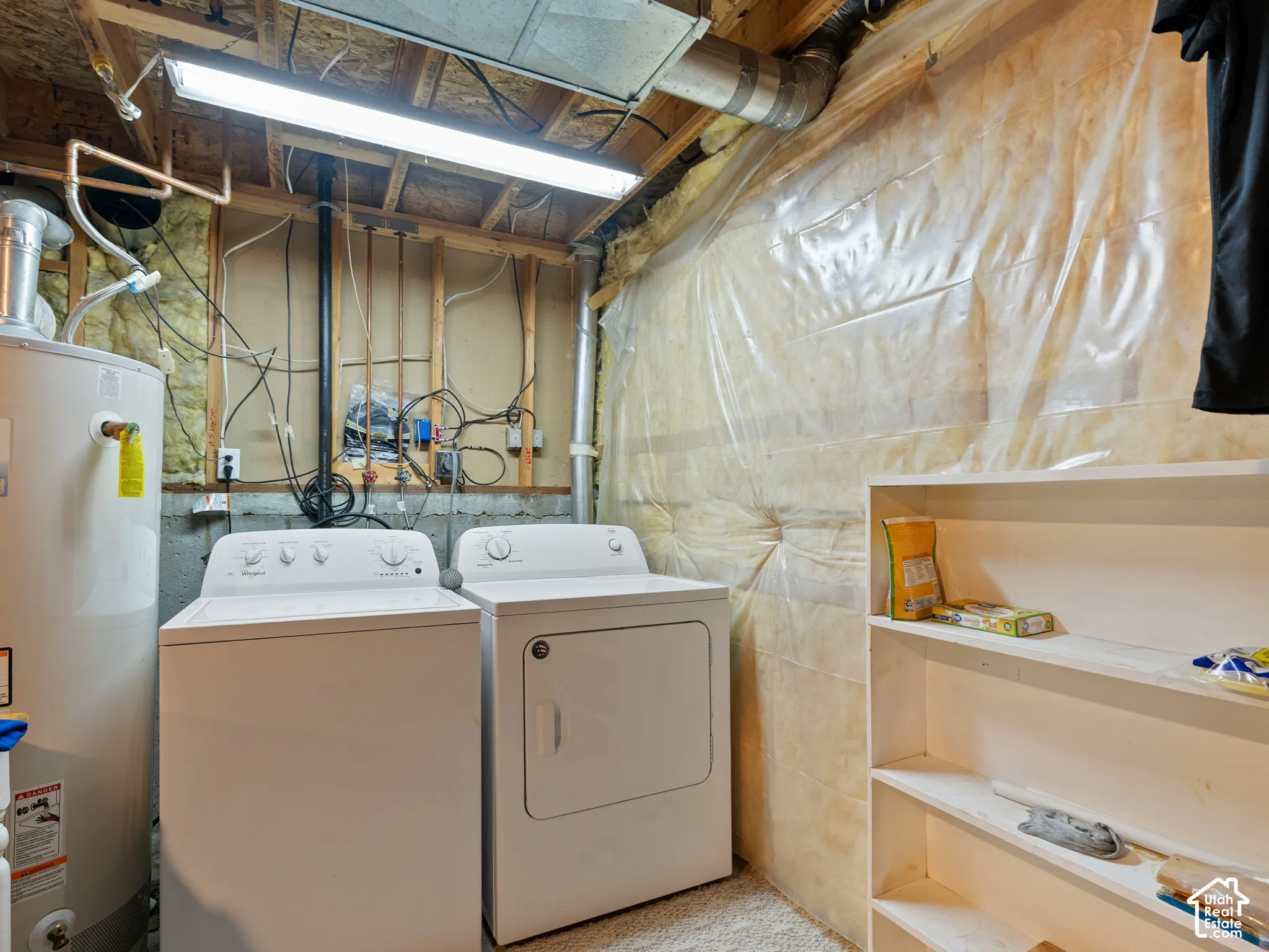 Laundry area featuring a top-load washing machine, front-load dryer, hot water heater, overhead fluorescent lighting, and built-in shelving