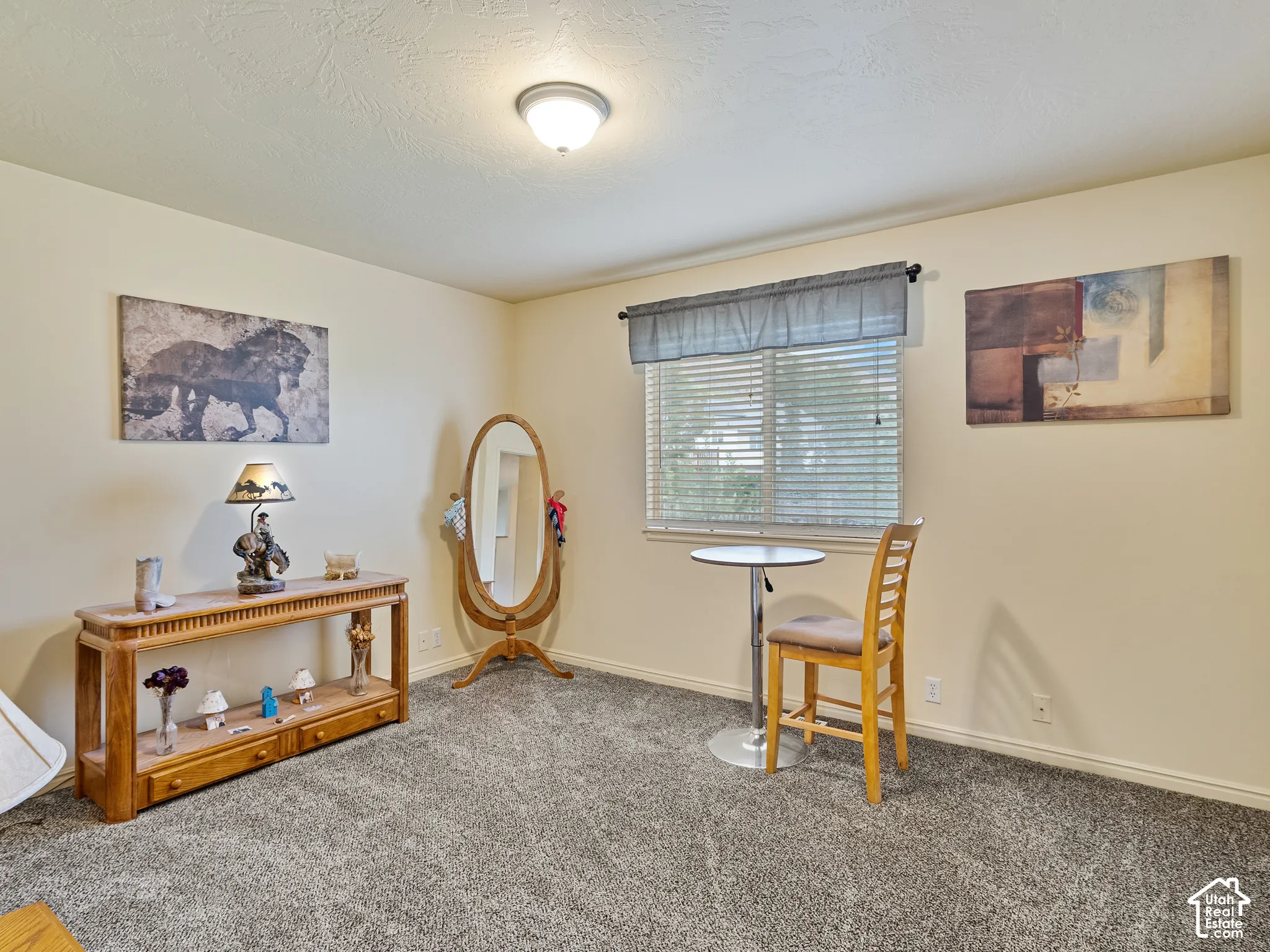 Neutral tone wall paint, textured ceiling, flush mount ceiling light fixture, window with blinds, and grey carpet flooring