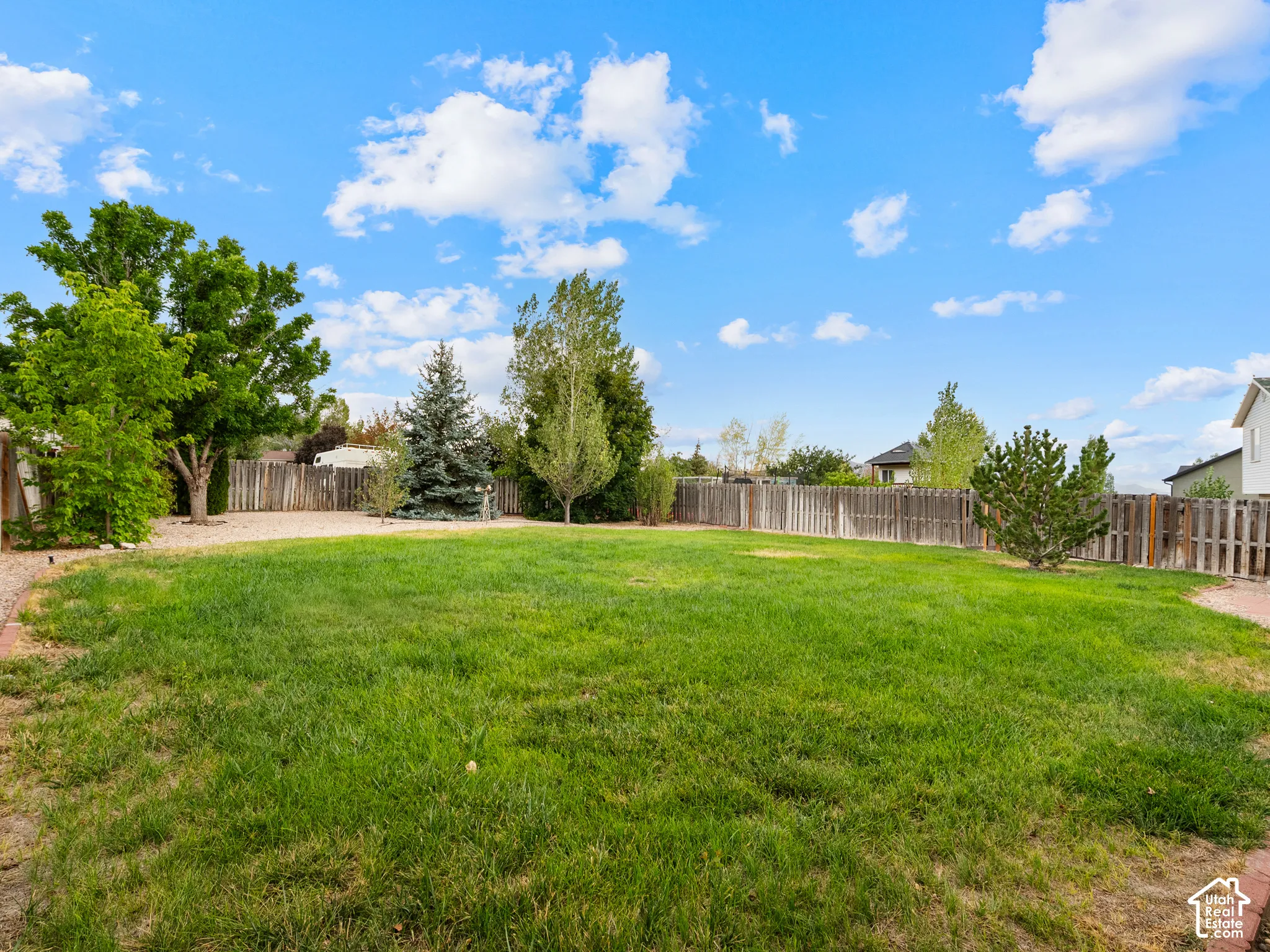 Expansive lawn area with a perimeter wood fence, mature trees, and a brick-lined border
