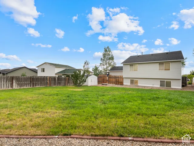 Spacious backyard featuring a grass lawn, privacy fencing, and a white storage shed