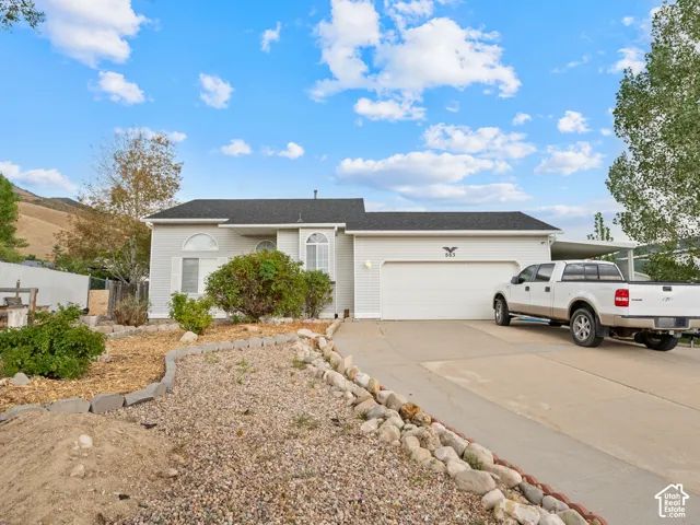 White vinyl siding, asphalt shingle roof, attached garage with white door, concrete driveway, and rock landscaping