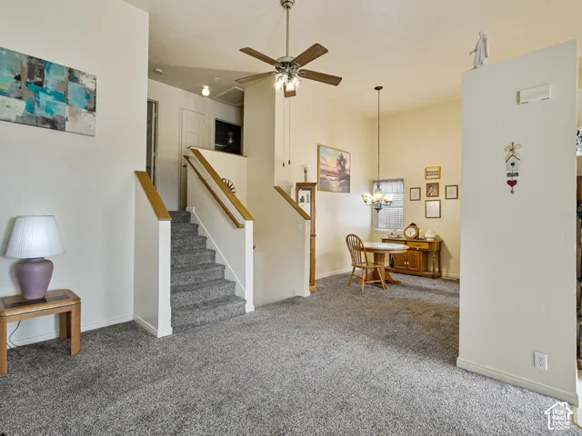 Carpeted flooring, staircase with wood-finish handrails, ceiling fan, and pendant lighting