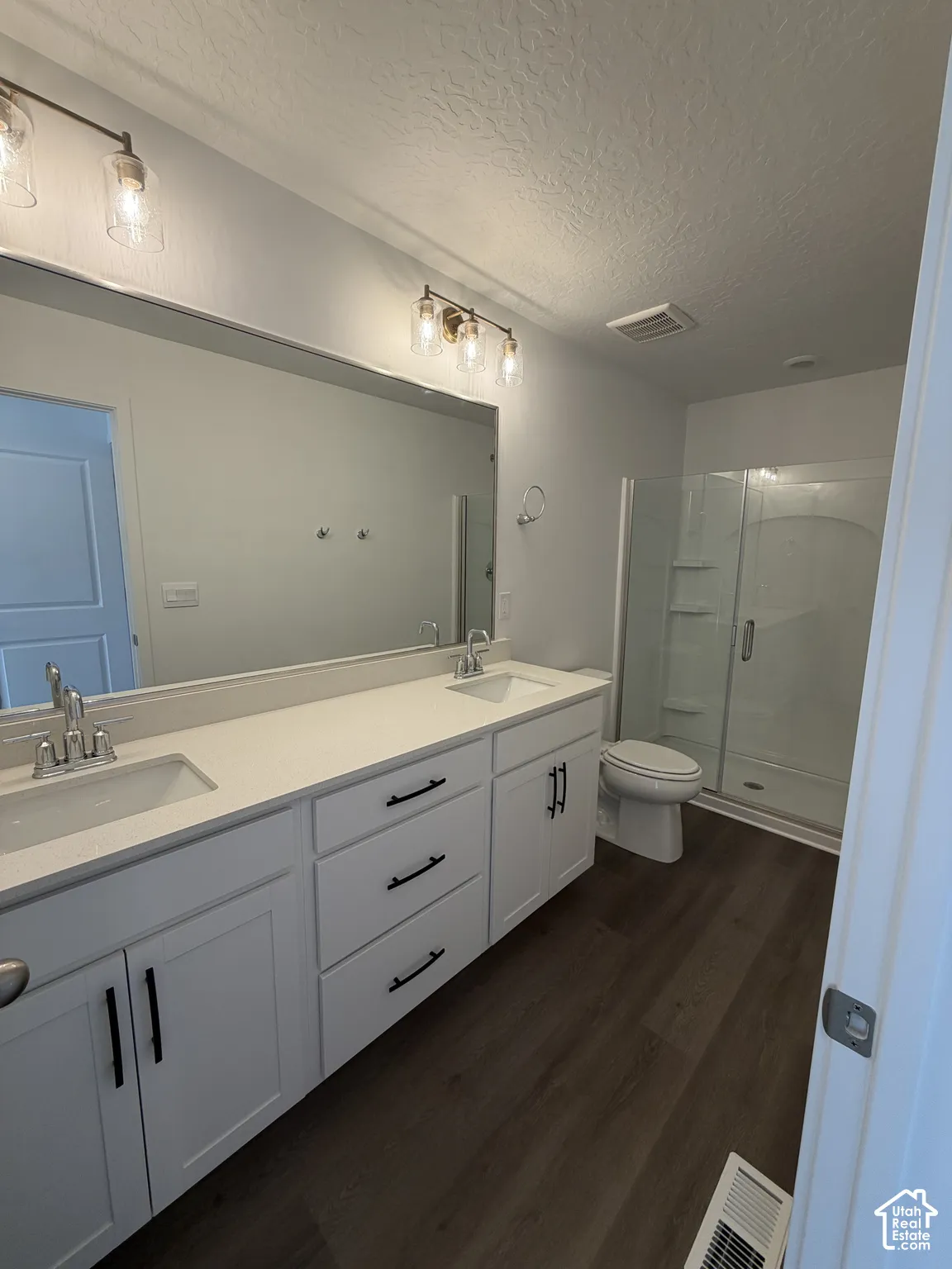 Double vanity with white cabinetry, wood-finish flooring, glass-enclosed shower, and modern lighting fixtures