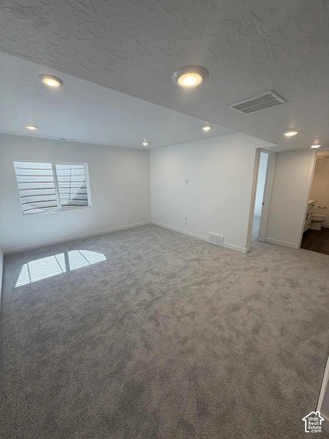 Spacious room featuring new carpet, recessed lighting, white walls, and a window with blinds