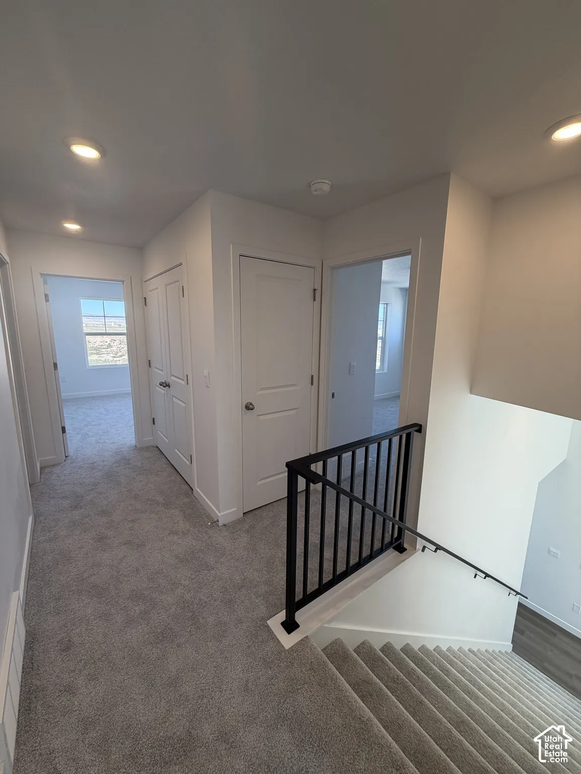 Recessed lighting illuminates the carpeted hallway and stairs, featuring a black metal railing