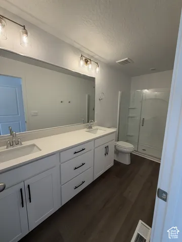 Double vanity with white cabinetry, wood-finish flooring, glass-enclosed shower, and modern lighting fixtures