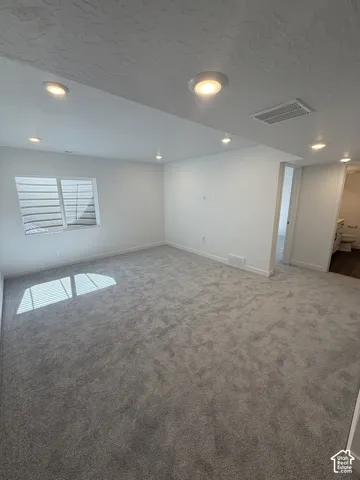 Spacious room featuring new carpet, recessed lighting, white walls, and a window with blinds