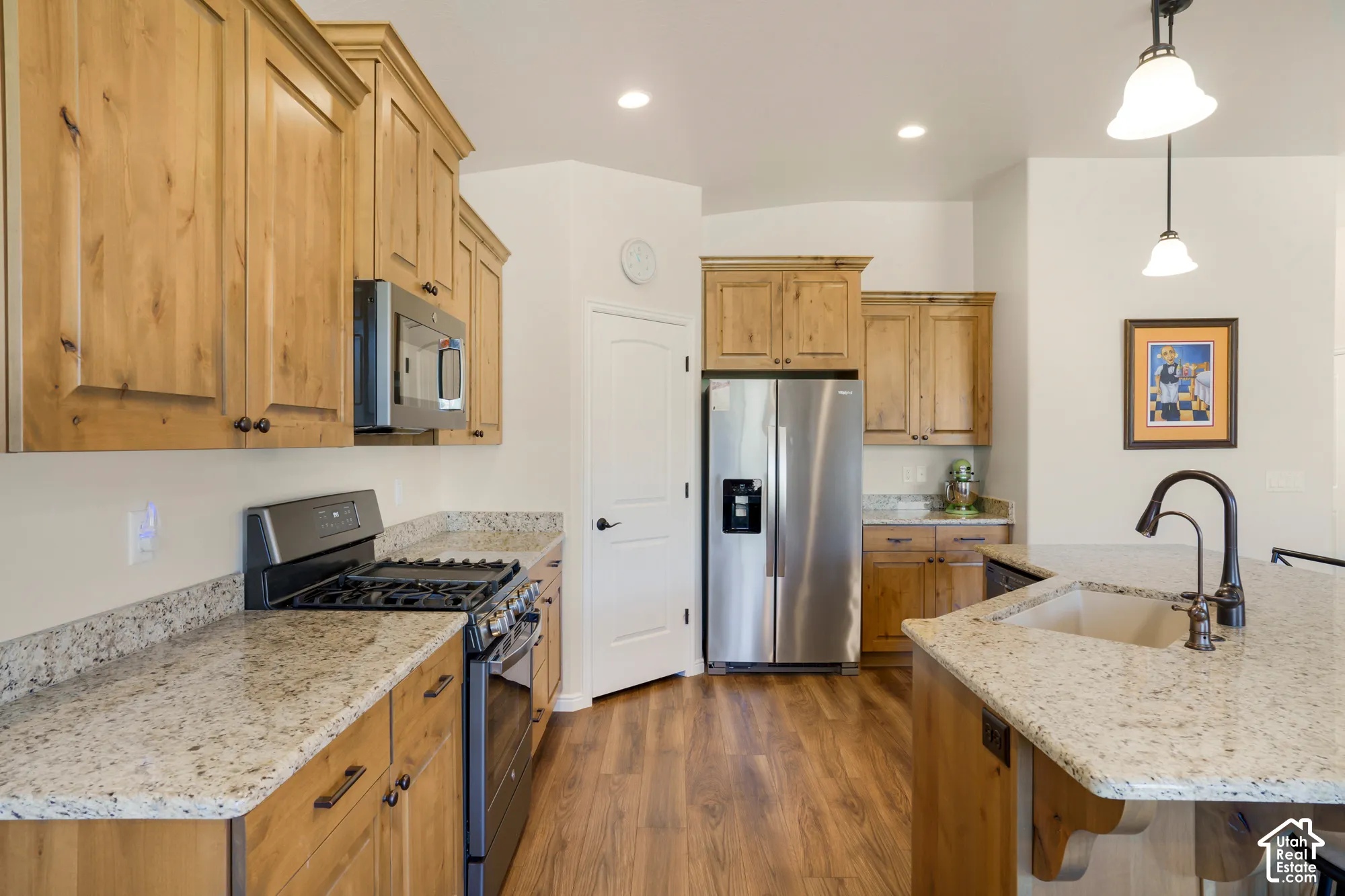 Spacious kitchen featuring warm wood cabinetry, stainless steel appliances including a gas cooktop and refrigerator with ice/water dispenser, granite countertops, an oversized island with seating area & pendant lighting
