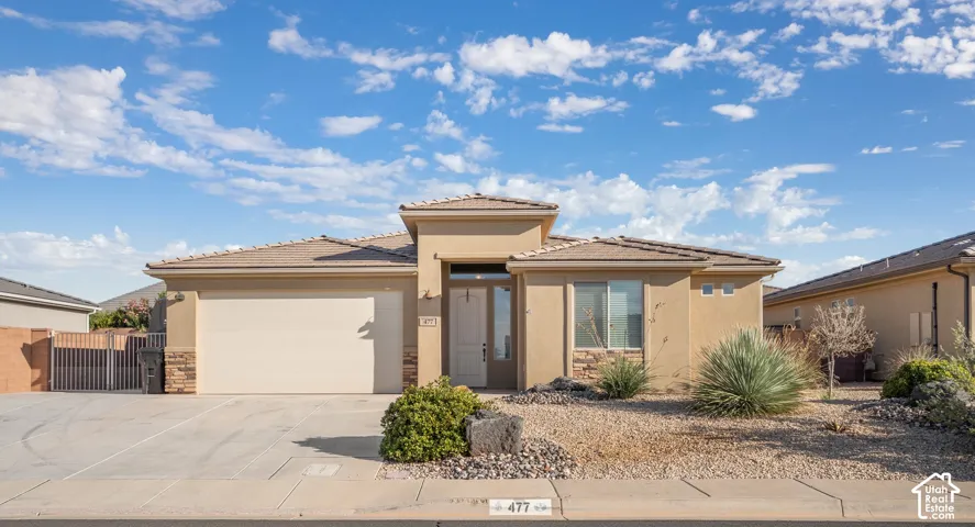 Stucco exterior featuring stone veneer accents, a tiled roof, a two-car garage, and desert-inspired landscaping
