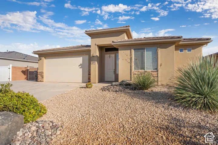 Stucco exterior featuring stone accents, a tile roof, an integrated garage, and a gravel front yard with desert landscaping