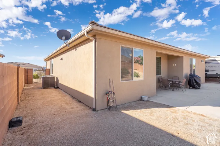 Stucco exterior with a covered patio, concrete hardscaping, and a gravel side yard