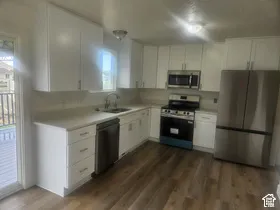 Wood-finish flooring, white cabinetry with silver hardware, light-toned countertops, stainless steel appliances, and a stainless steel sink with a gooseneck faucet