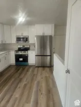 Modern kitchen featuring white cabinetry, stainless steel appliances, light-toned countertops, and wood-finish flooring