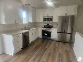 Kitchen featuring white cabinetry, light countertops, wood-finish flooring, stainless steel appliances, and a window above the sink
