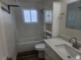Wood-finish flooring, white vanity with integrated sink, light-toned countertop, wall-mounted mirror, and white built-in storage cabinet