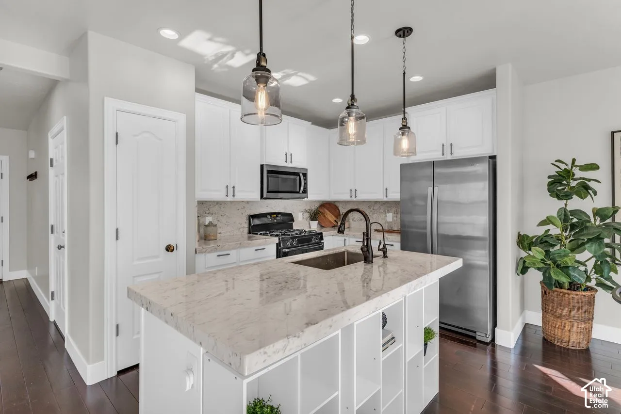 Kitchen featuring white cabinetry, updated glass pendant lights, marble counters and matching backsplash, and stainless appliances.
