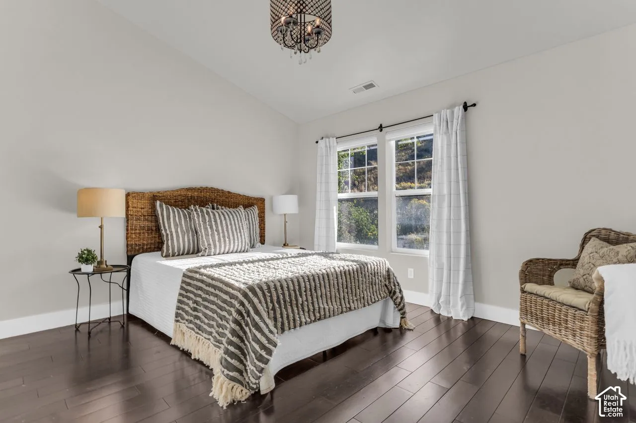 Spacious primary bedroom with updated light fixture, vaulted ceilings, and hardwood flooring